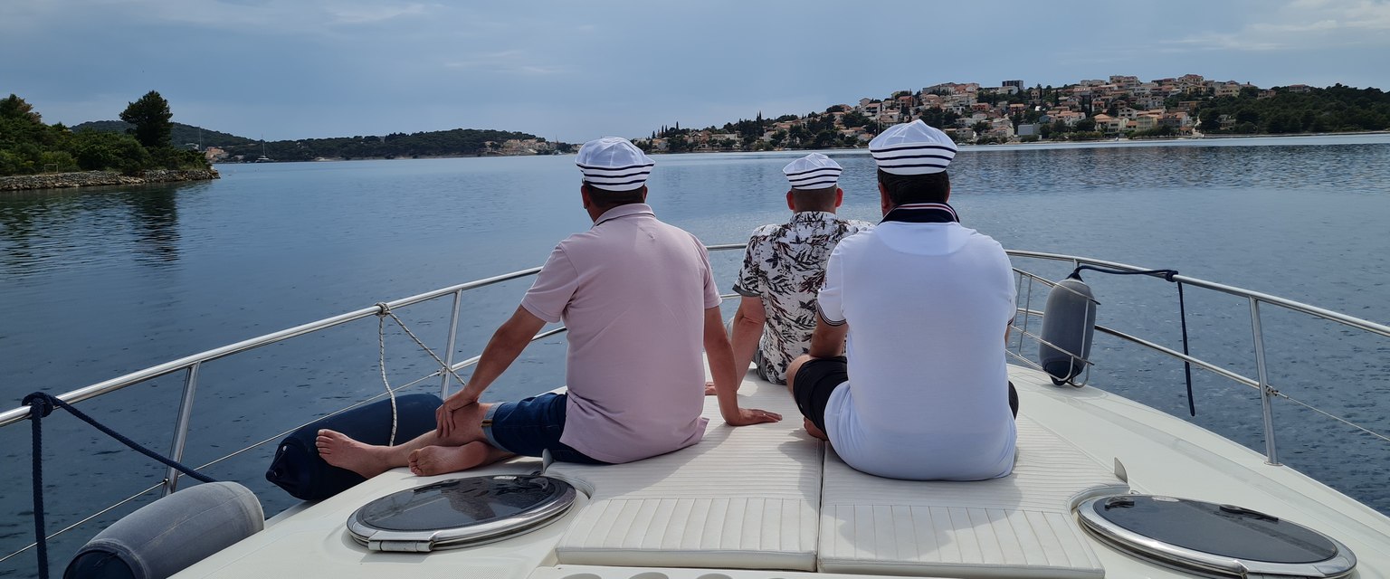 Drei Personen sitzen auf dem Vordeck eines Motorboots und blicken über die Bucht auf eine Ortschaft