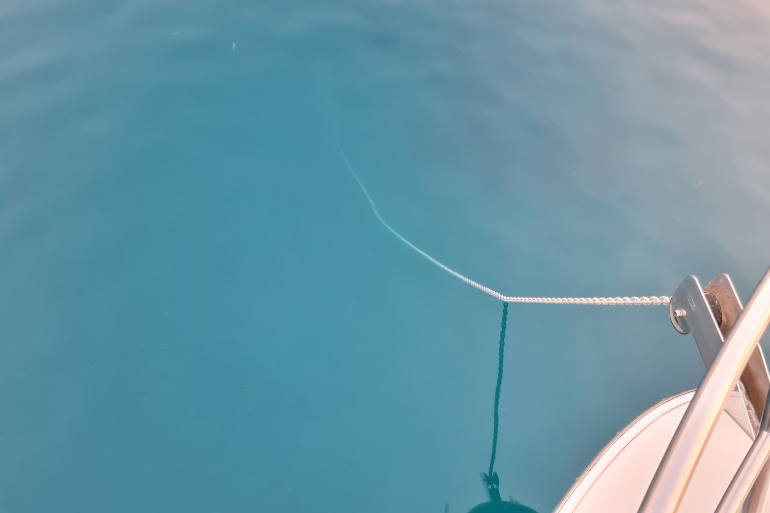 Ankerleine an der Bugklampe eines Motorboots, darunter klares türkisfarbenes Wasser