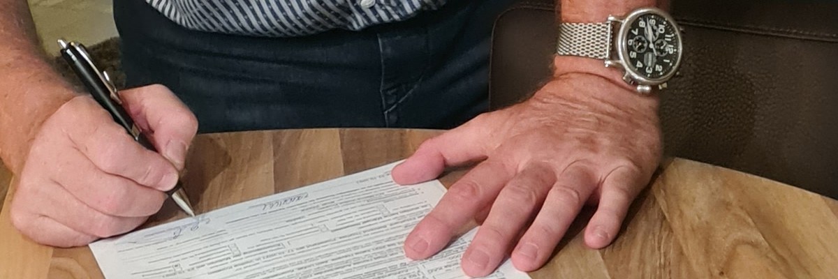 Zwei Hände und ein Stift über einem Kaufvertrag auf einem Holztisch